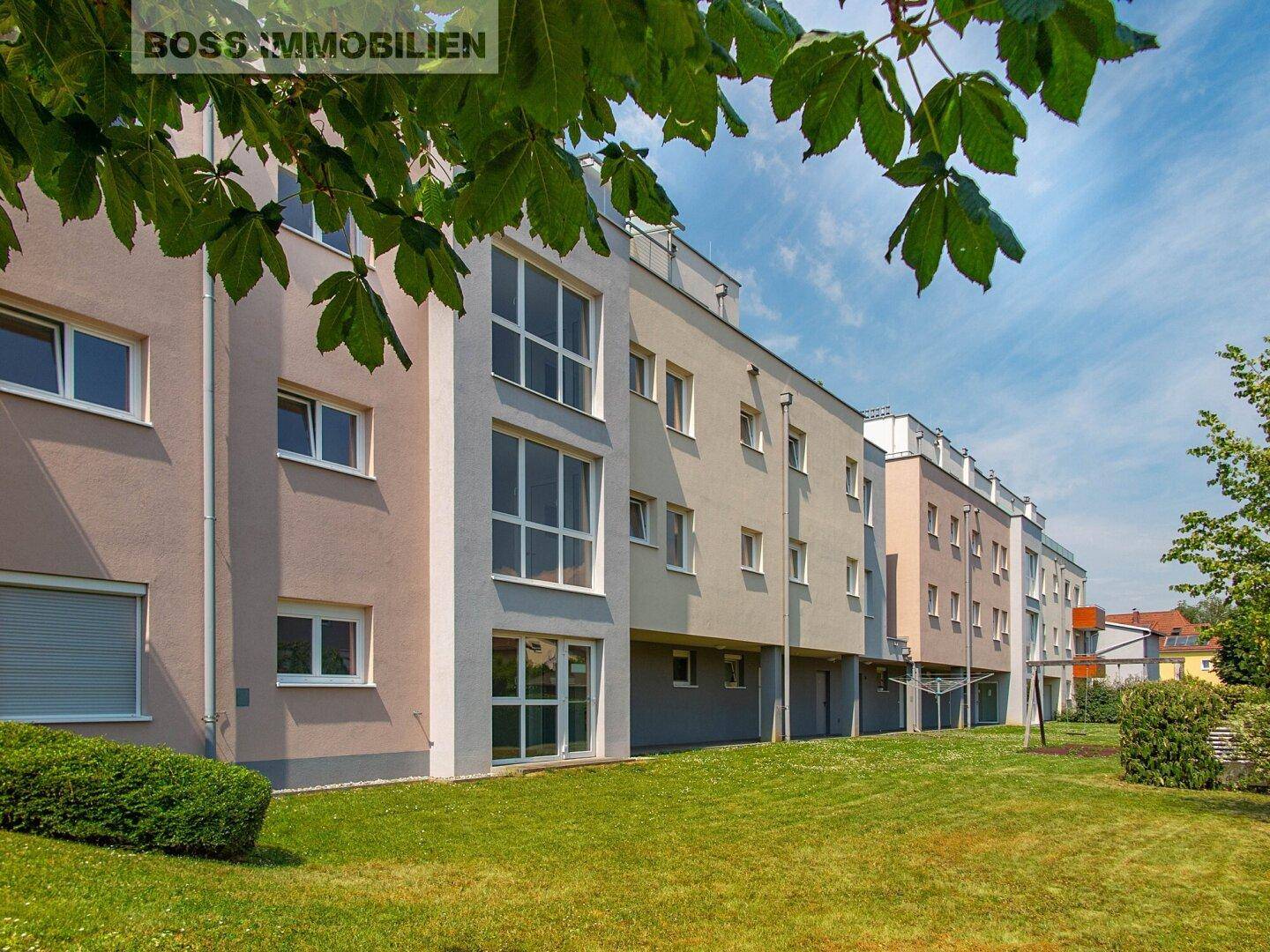 Rückseite der Wohngebäude mit großer Rasenfläche und Bäumen unter blauem Himmel.
