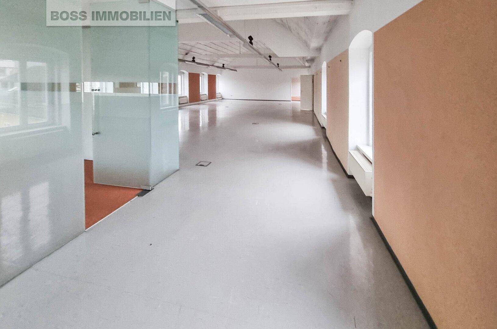 Langer, leerer Büroraum mit glänzendem Boden, Glaswänden und Fenstern entlang der Seite.