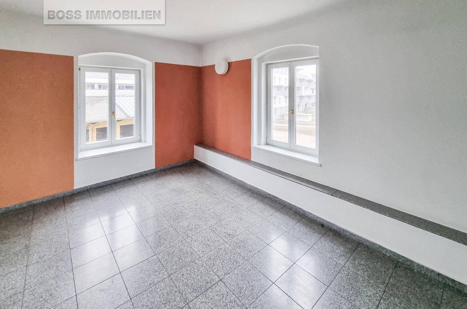 Kleiner Büroraum mit zwei Fenstern, Terrazzoboden und Wänden in Weiß und Terrakotta.