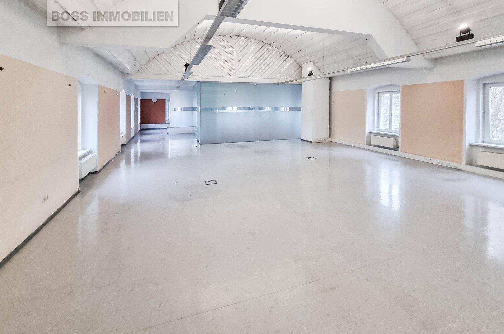 Großer, leerer Büroraum mit hohen Gewölbedecken, Glaswänden und glänzendem Betonboden.
