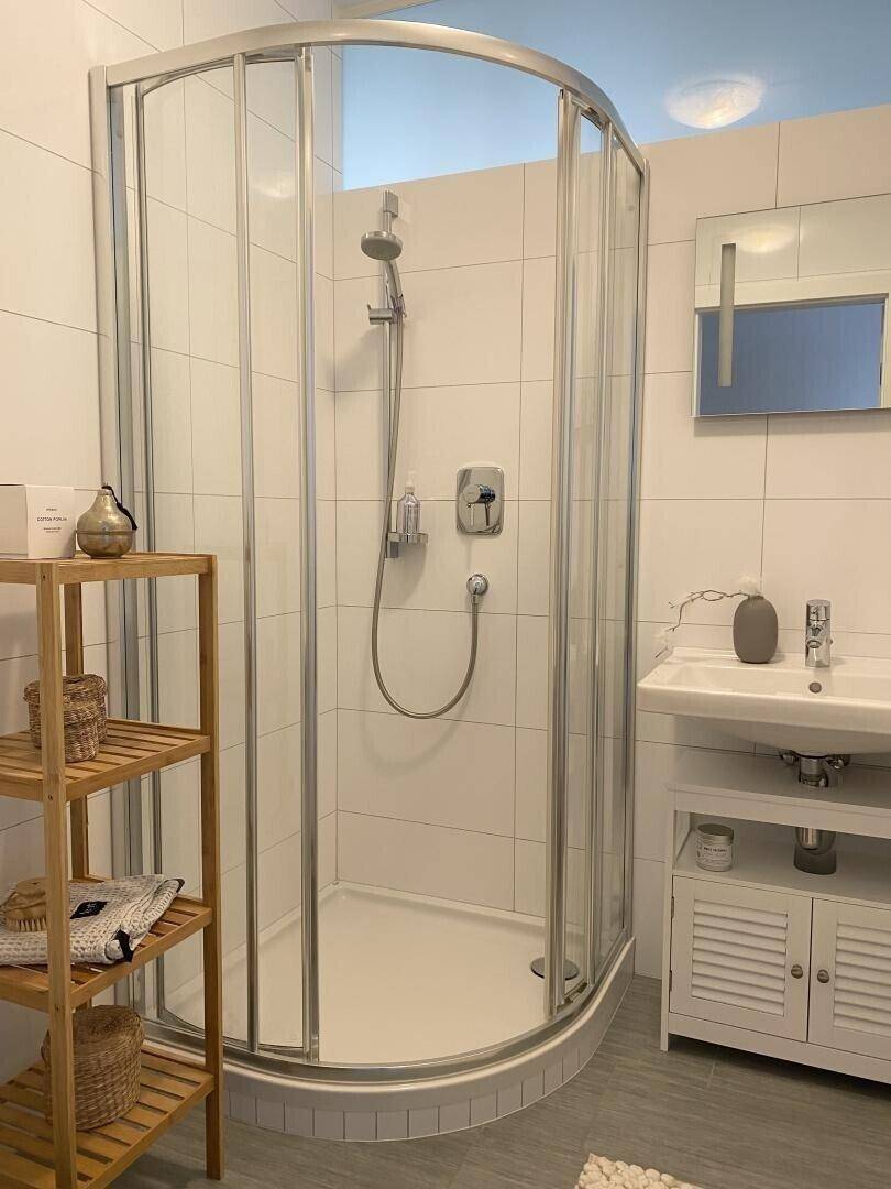 Modernes Badezimmer mit Duschkabine, weißen Fliesen und Holzregal.