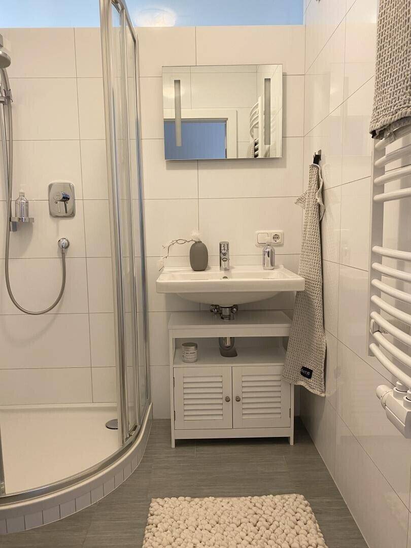 Helles Badezimmer mit Dusche, Waschbecken und beheiztem Handtuchhalter.