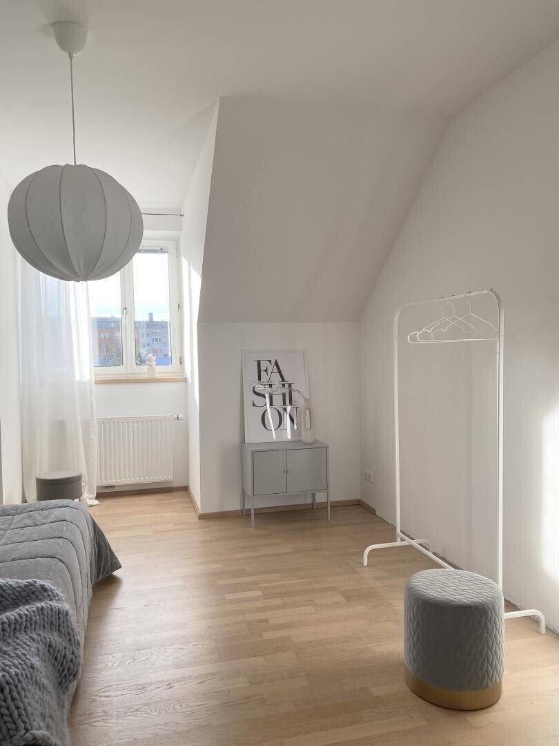 Helles Schlafzimmer mit Fenster, das viel Tageslicht hereinlässt und Holzboden.