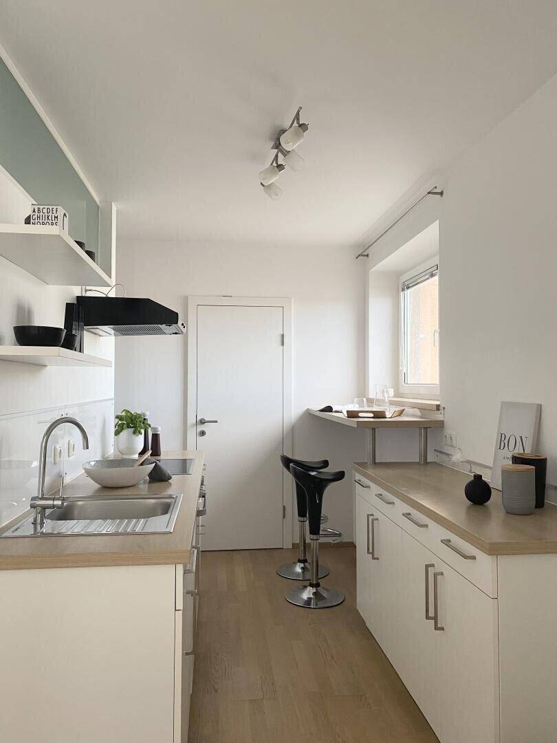 Moderne Küche mit hellen Holzoberflächen, integrierten Geräten und Fenster.