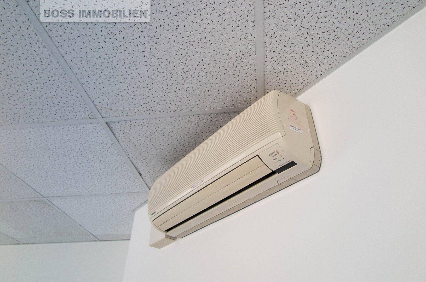 Nahaufnahme einer Klimaanlage an der Wand eines Büroraums mit Rasterdecke.