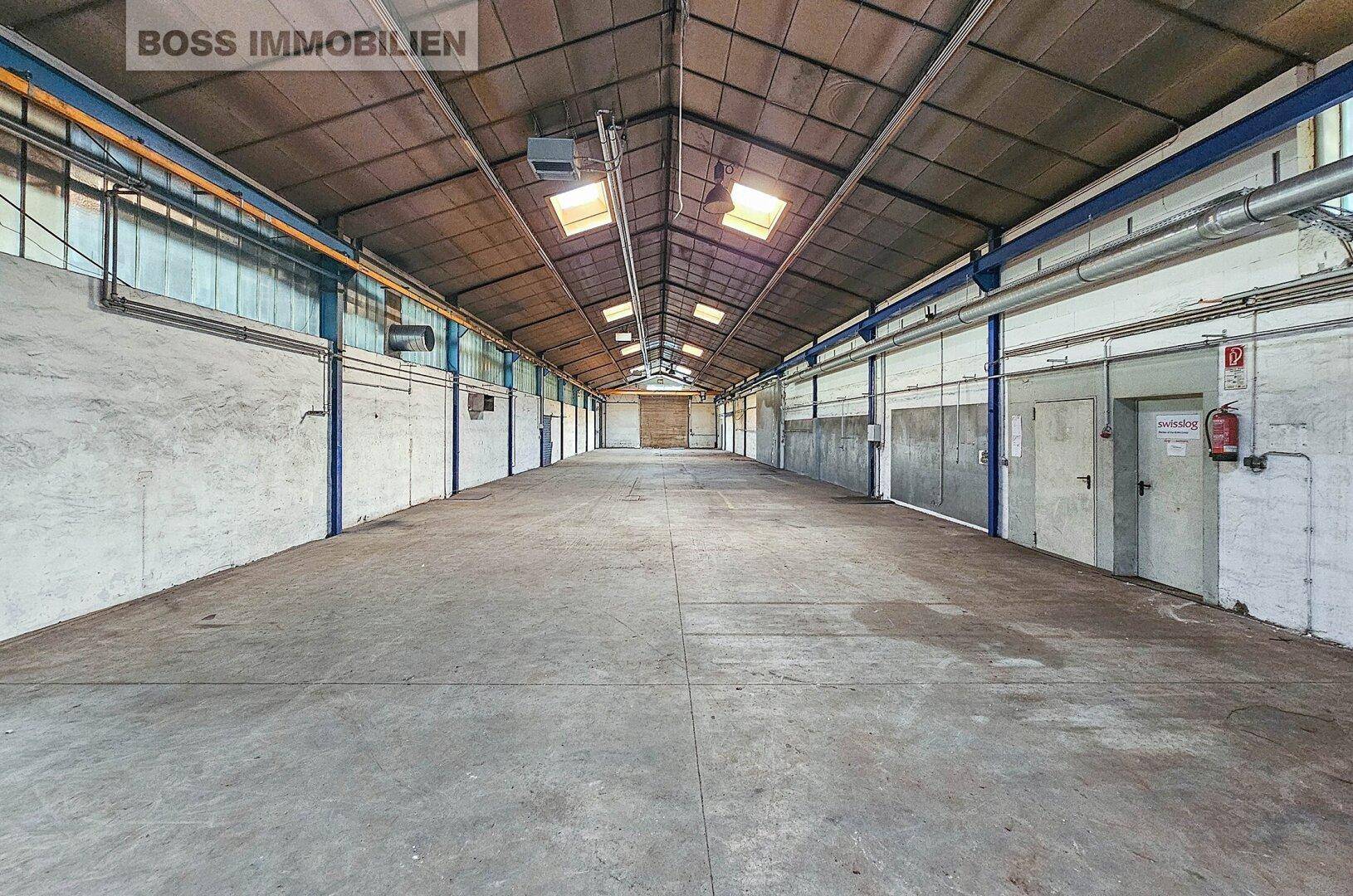 Weitläufige Lagerhalle mit Betonboden und Oberlichtern, die viel natürliches Licht hereinlassen.