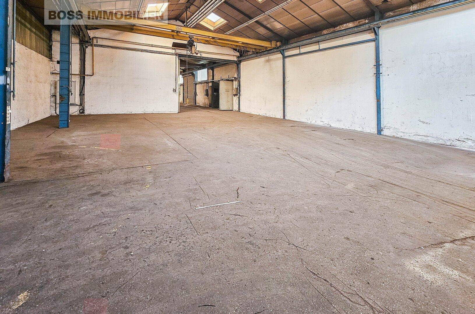 Blick auf den robusten Betonboden und die Wände einer geräumigen Lagerhalle mit industriellem Charme.