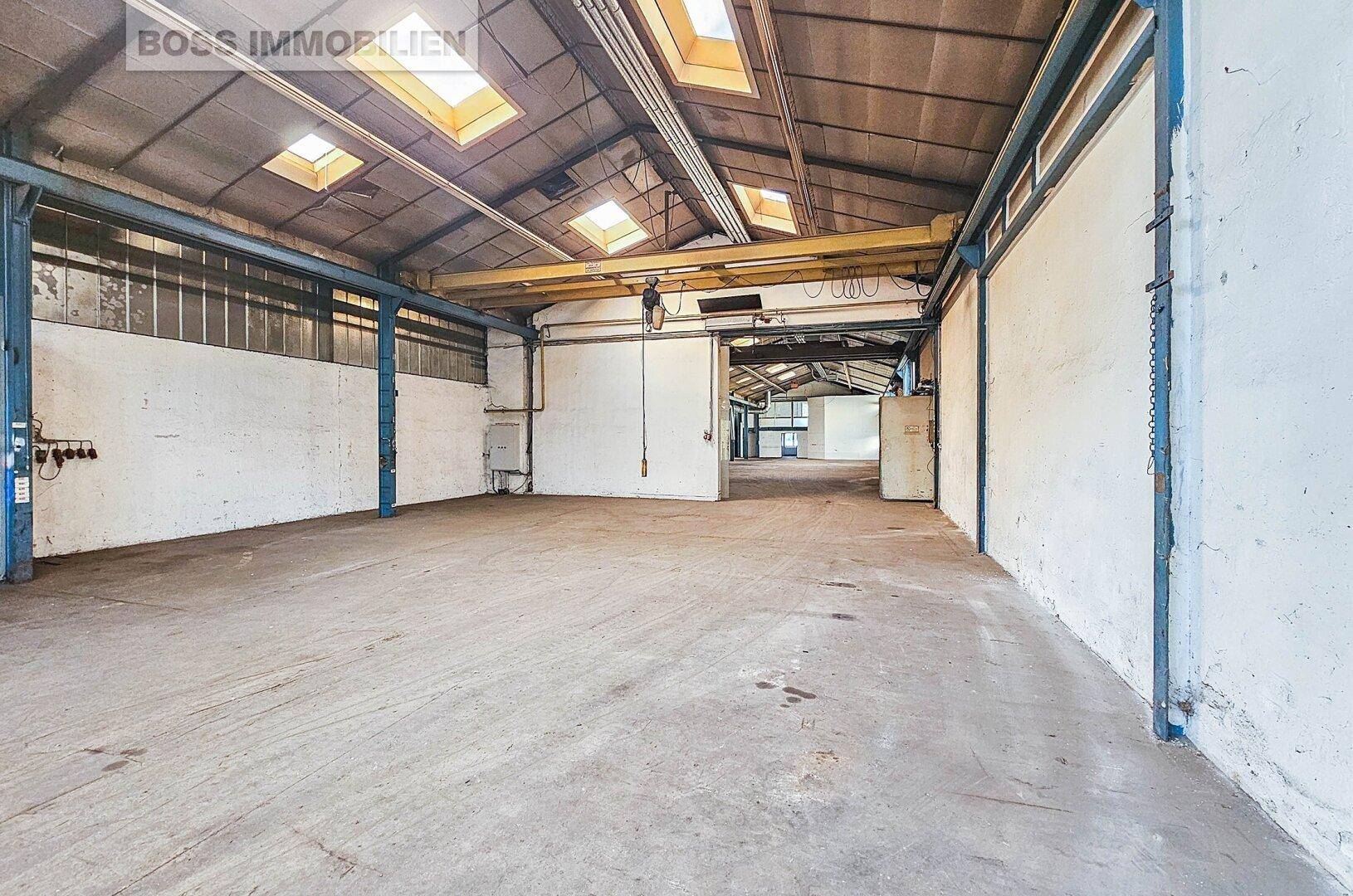Große, leere Lagerhalle mit Betonboden, hohen Decken und natürlichem Lichteinfall durch Oberlichter.