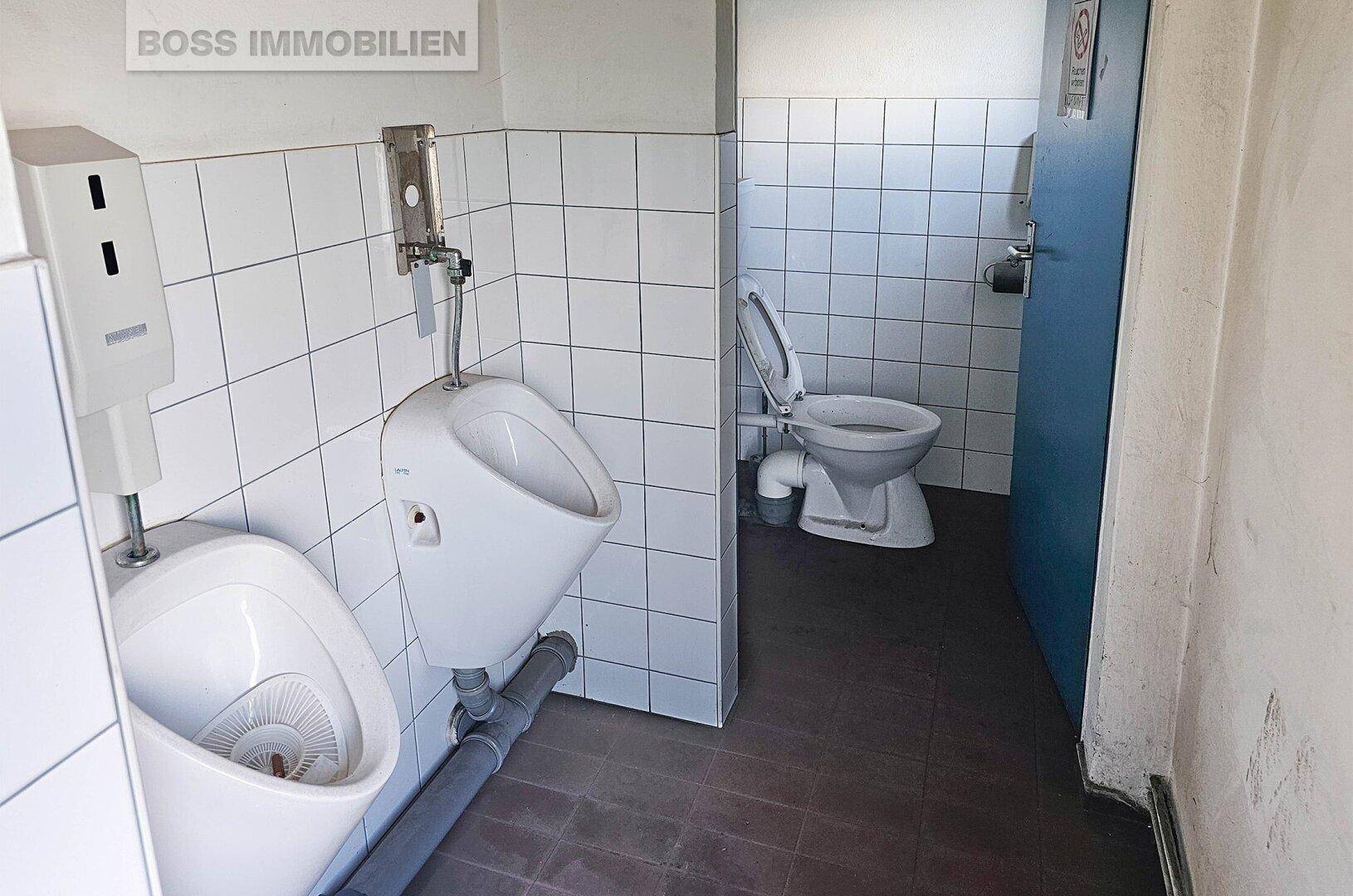 Herren-WC mit zwei Urinalen und einer Toilette, ausgestattet mit weißen Fliesen.