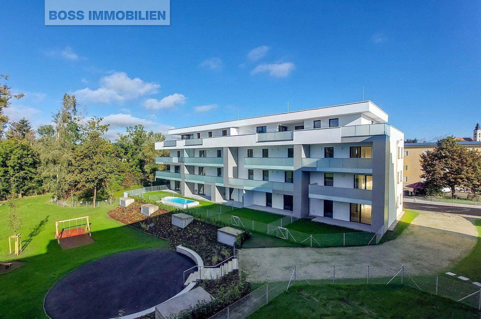 Luftaufnahme einer modernen Wohnanlage mit Pool, Spielplatz und viel Grünfläche.