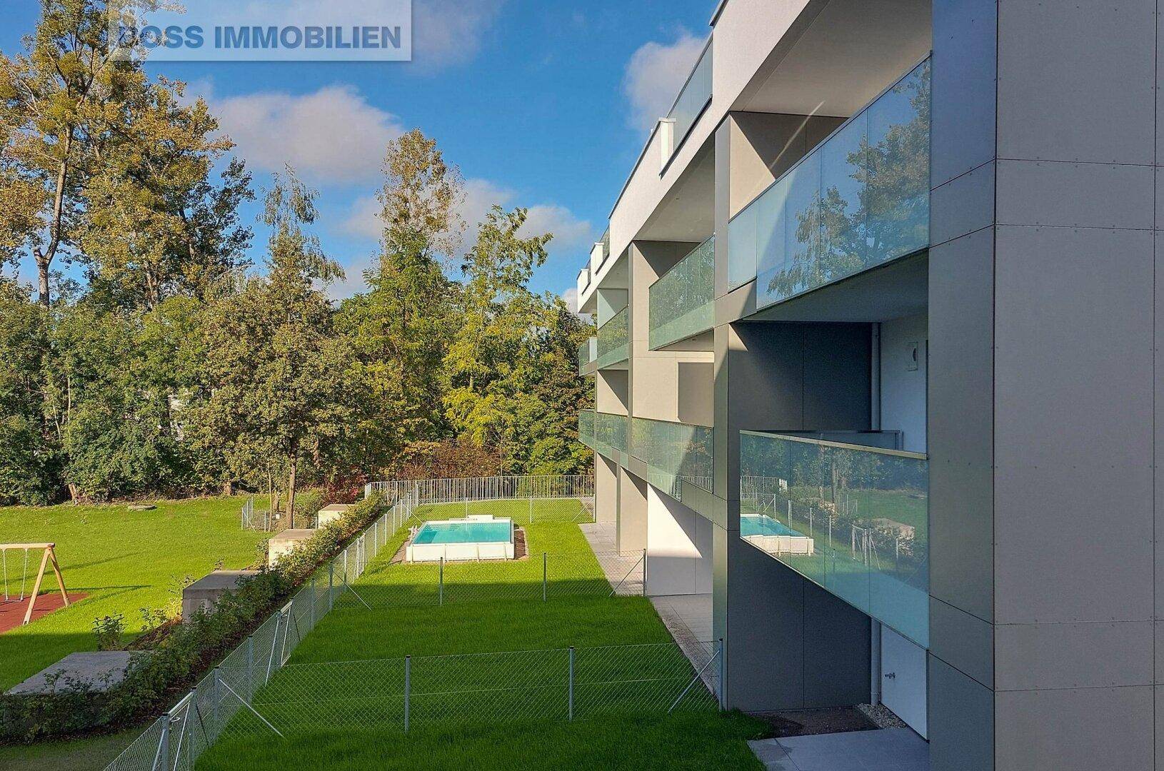 Seitenansicht der modernen Wohnanlage mit Balkonen, Pool und angrenzendem Spielplatz.