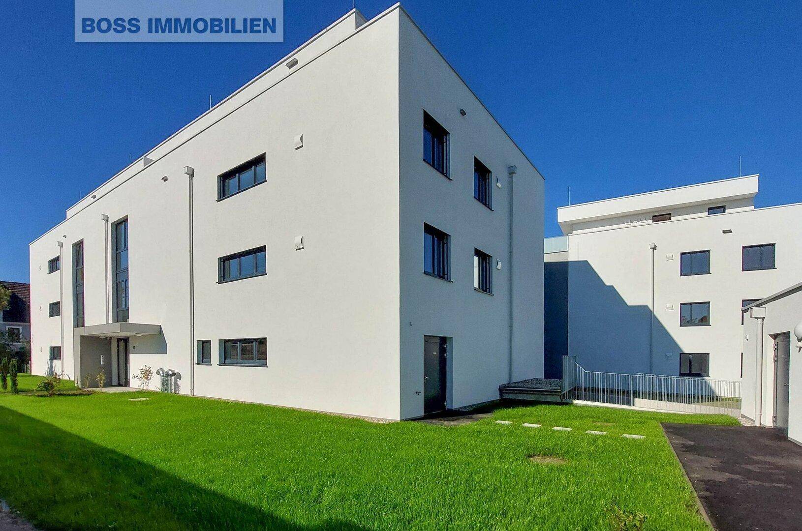 Modernes weißes Gebäude mit klaren Linien und einer gepflegten grünen Rasenfläche.