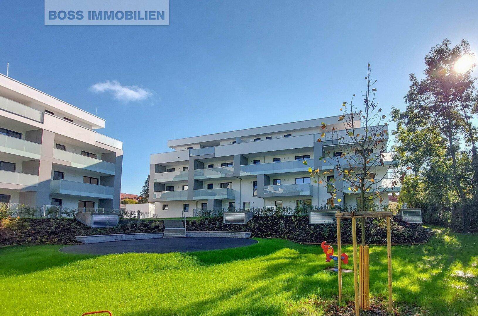 Zwei moderne Wohngebäude mit gepflegter Grünfläche und einem Spielbereich im Vordergrund.