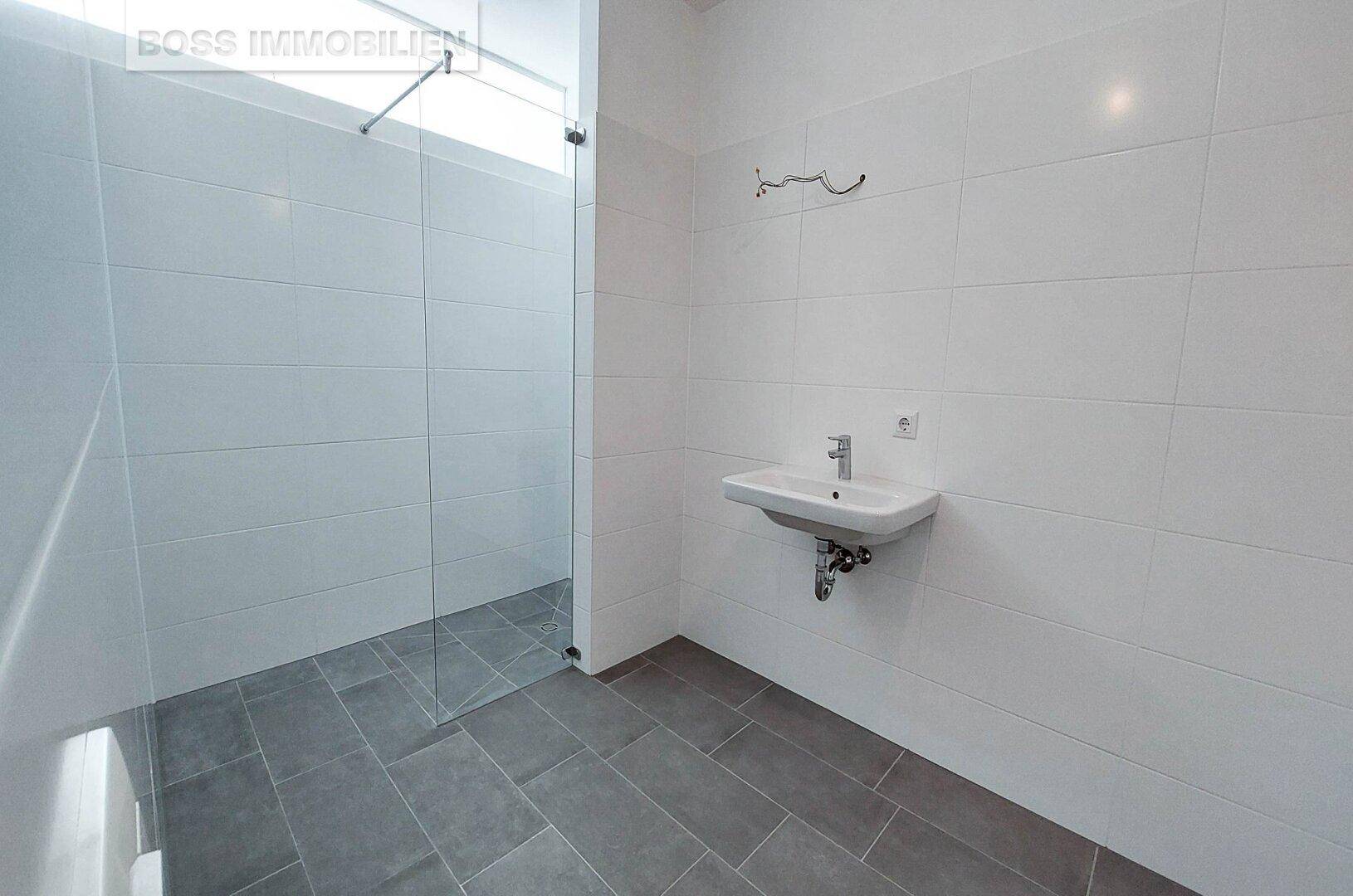 Modernes Badezimmer mit ebenerdiger Dusche, weißen Fliesen und einem einzelnen Waschbecken.