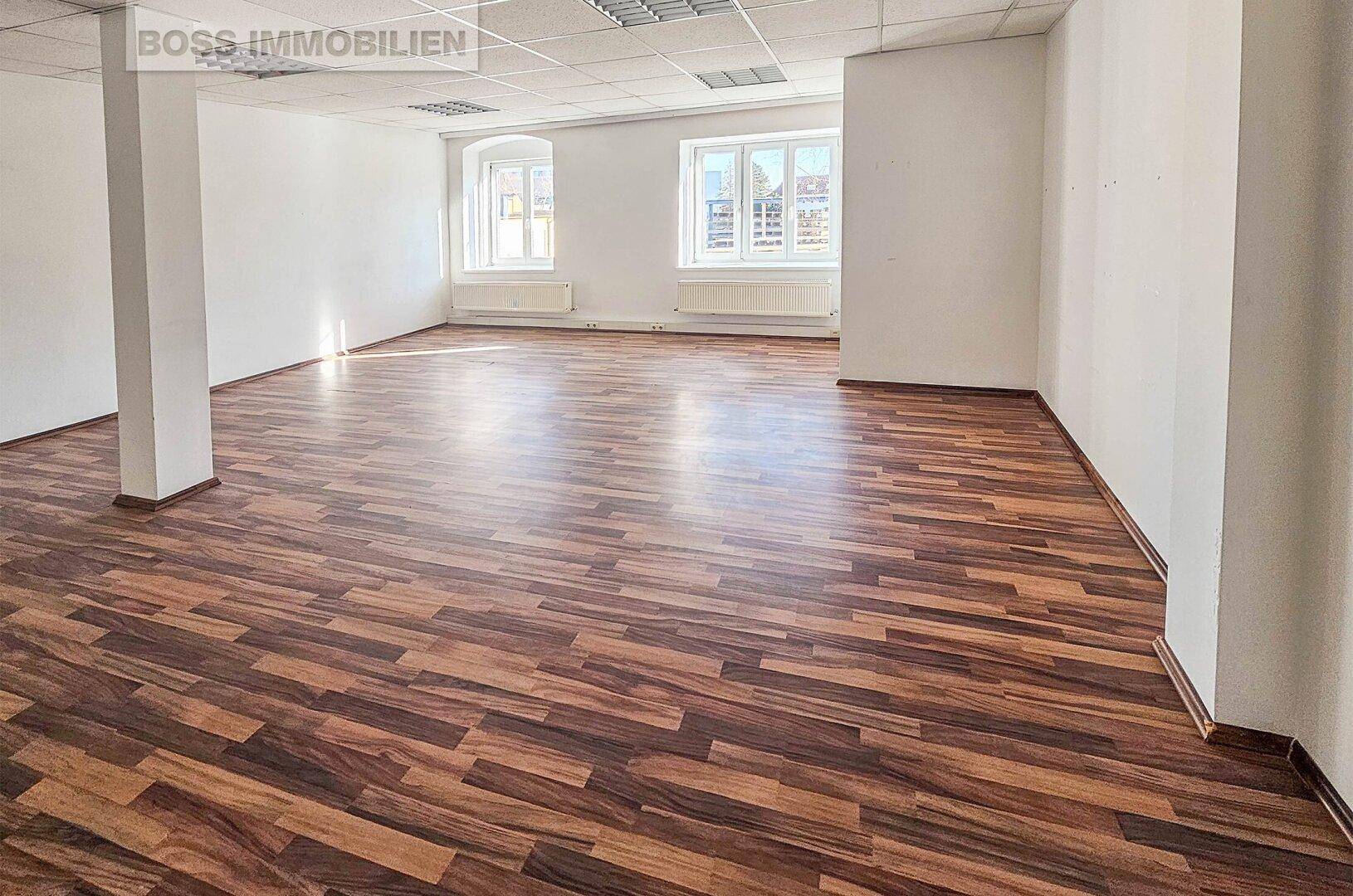 Großer, heller Büroraum mit Laminatboden und weißen Wänden, ideal für verschiedene Nutzungen.