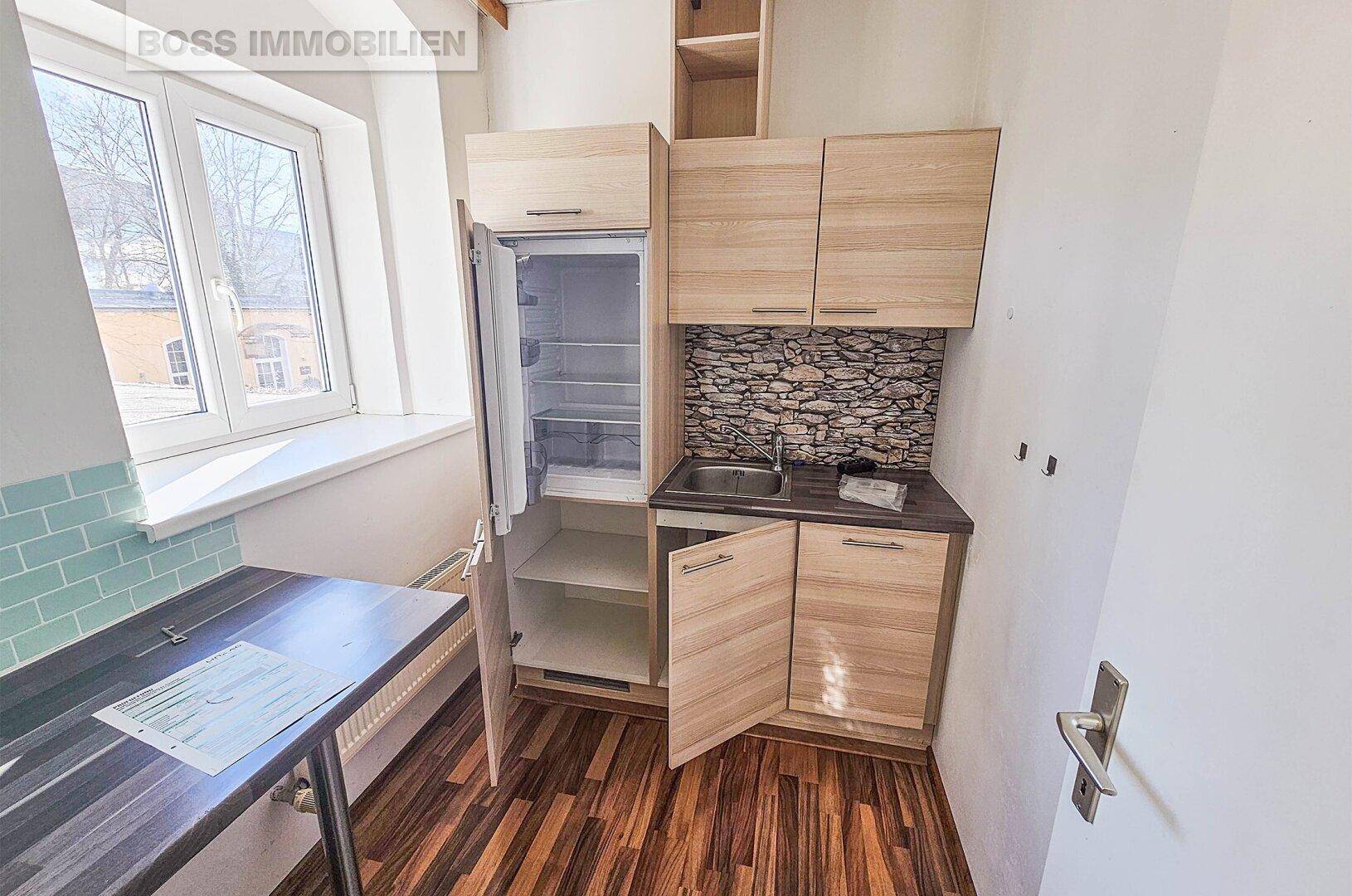 Kleine Küchenzeile mit Holzschränken, Spüle und Kühlschrank, ideal für eine Büroküche.