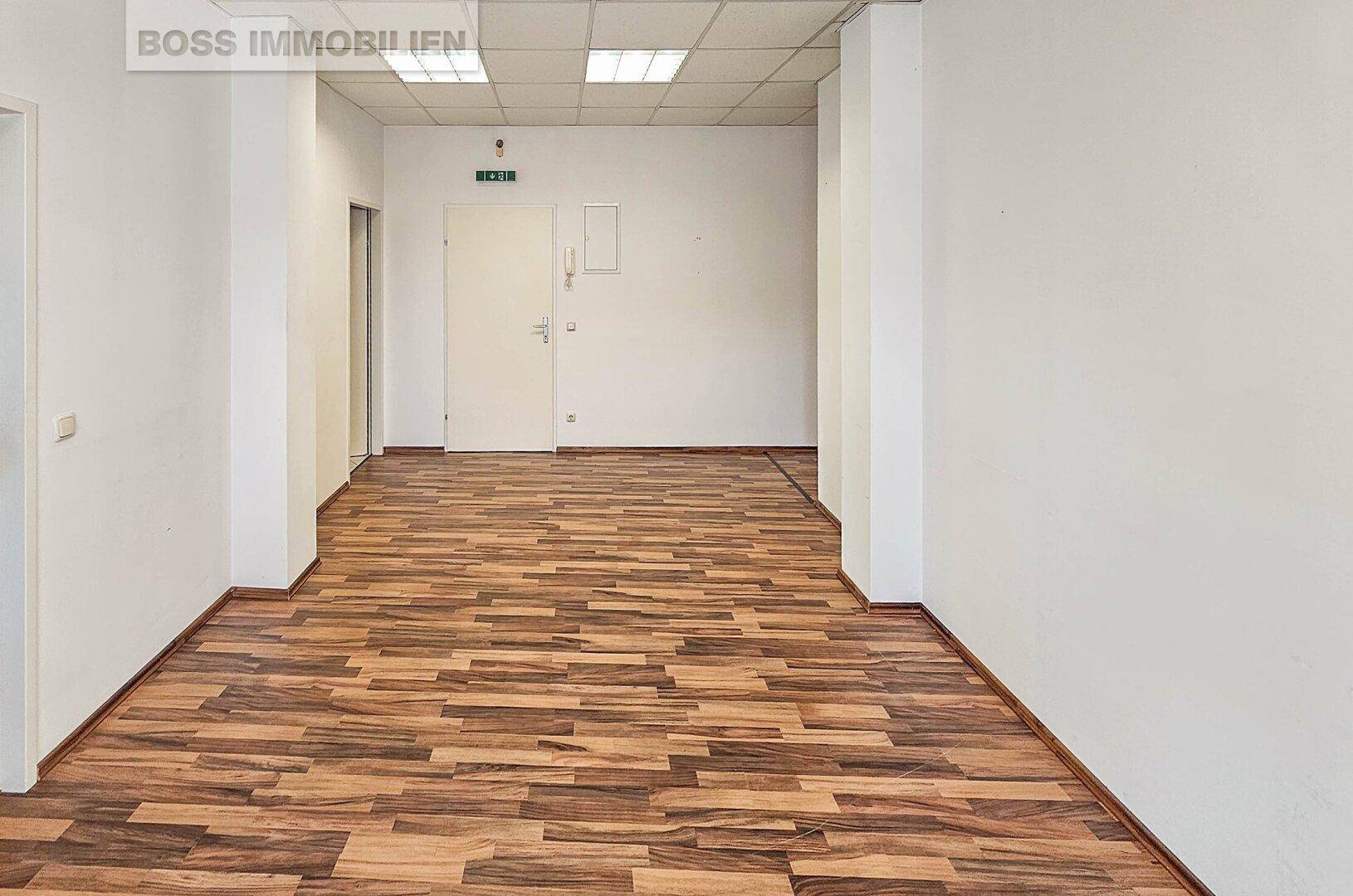 Langer Flur mit Laminatboden und weißen Wänden, der zu weiteren Räumen führt.