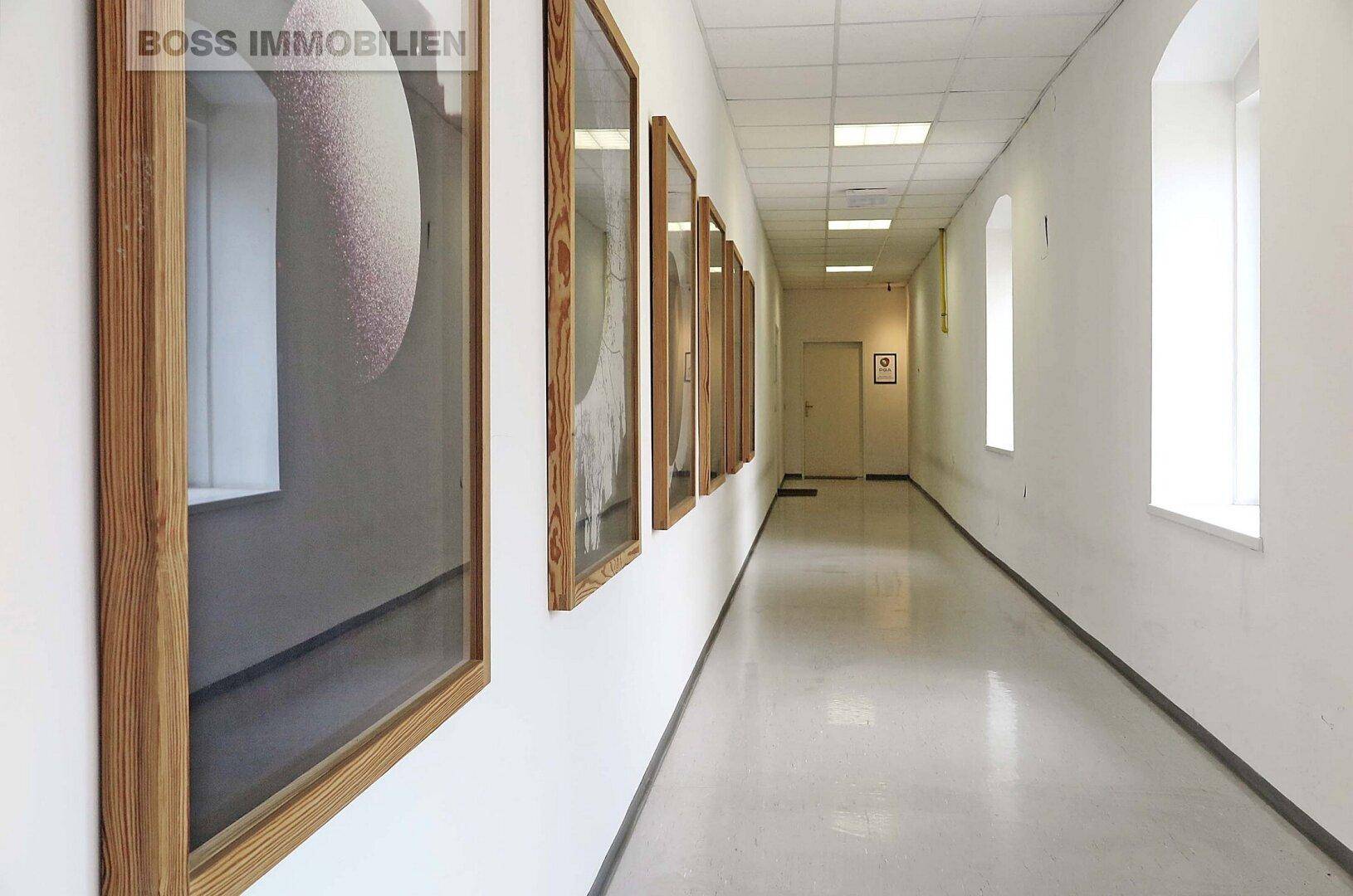 Langer, heller Flur mit Kunstwerken an der Wand und Fenstern, die Tageslicht spenden.