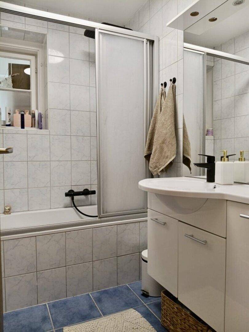 Funktionales Badezimmer mit Badewanne, Duschabtrennung, Waschbecken und Fenster.