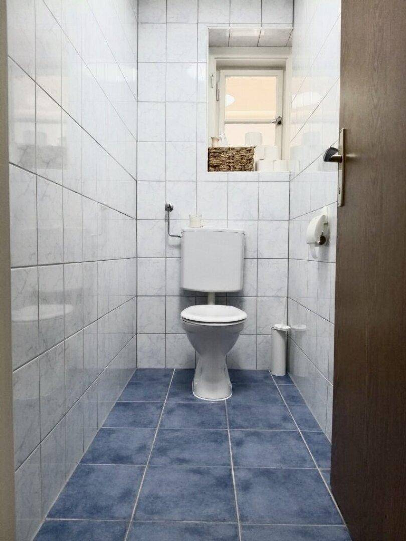 Separates WC mit Fliesenboden, Toilette und kleinem Fenster für Belüftung.