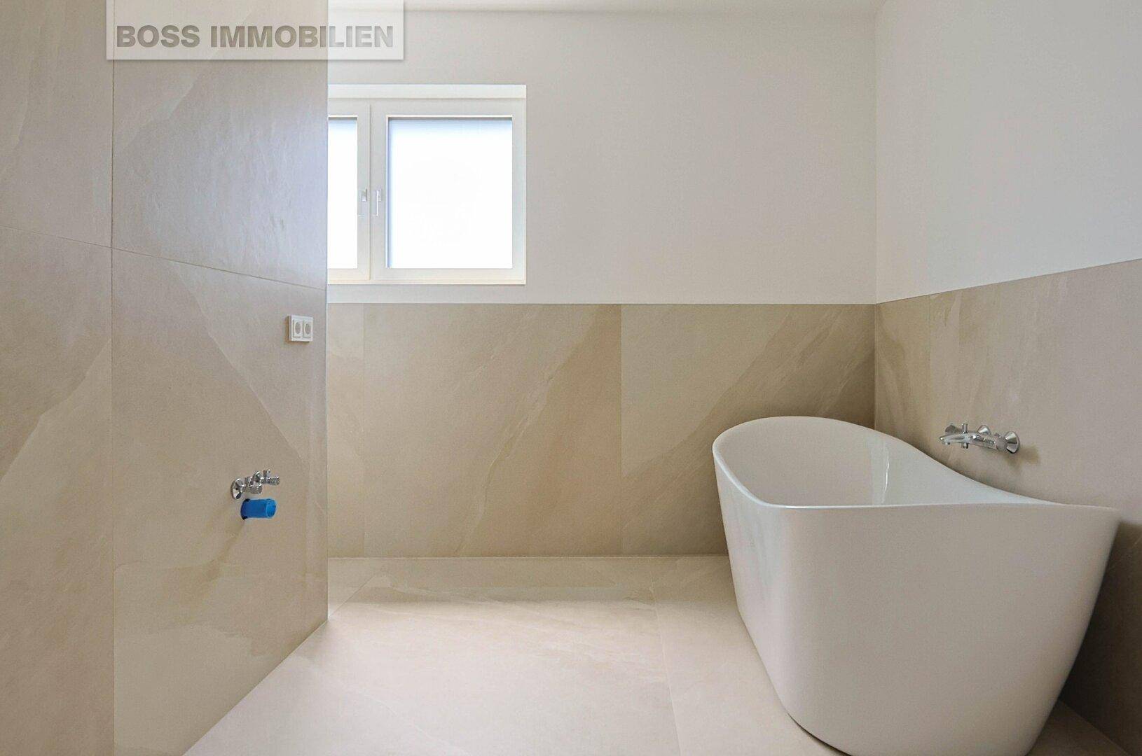 Modernes Badezimmer mit freistehender Badewanne, Fenster und beigefarbenen Fliesen.