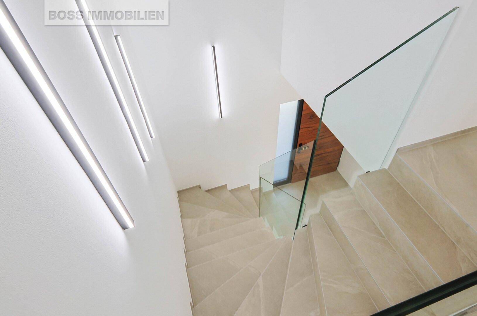 Blick von oben auf eine moderne Treppe mit Glasgeländer und indirekter Beleuchtung.