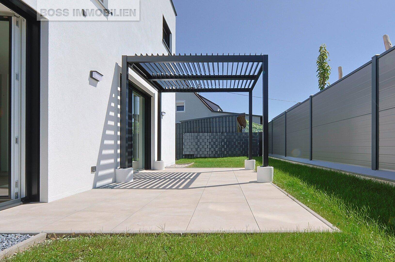 Terrasse mit Pergola und Zugang zu einer gepflegten Rasenfläche am Haus.