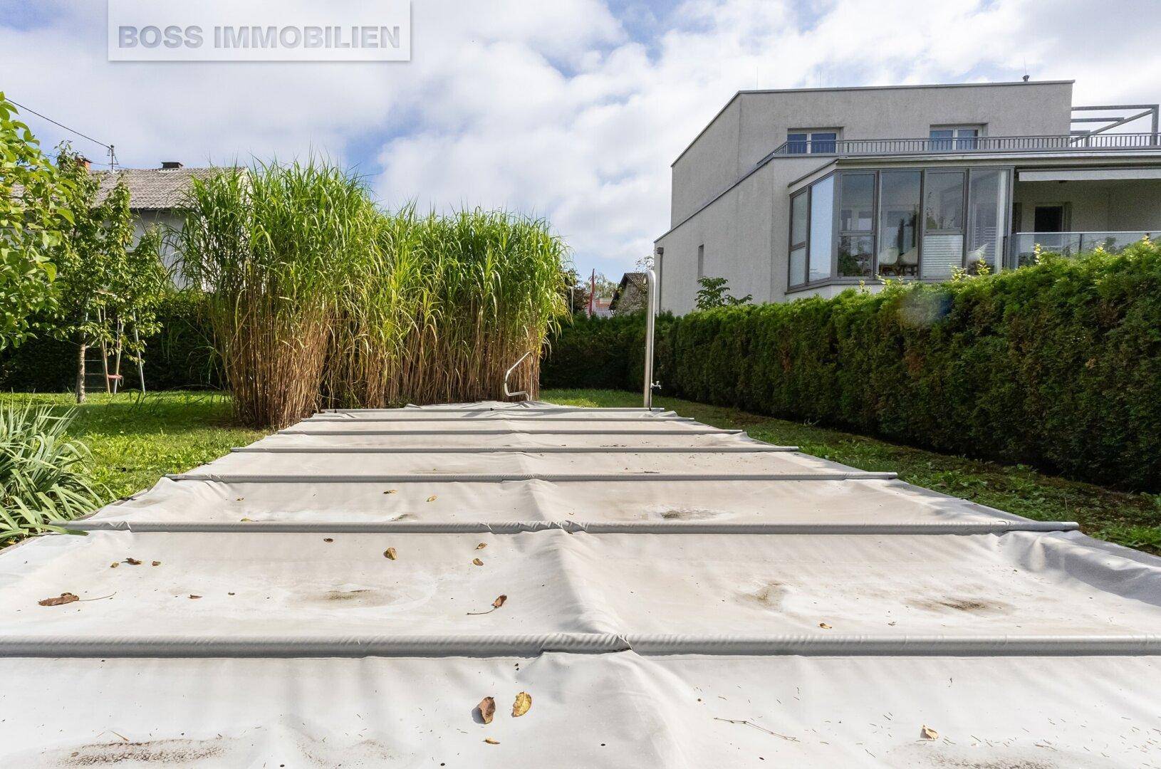 Großer Gartenbereich mit abgedecktem Pool und hoher Bepflanzung.