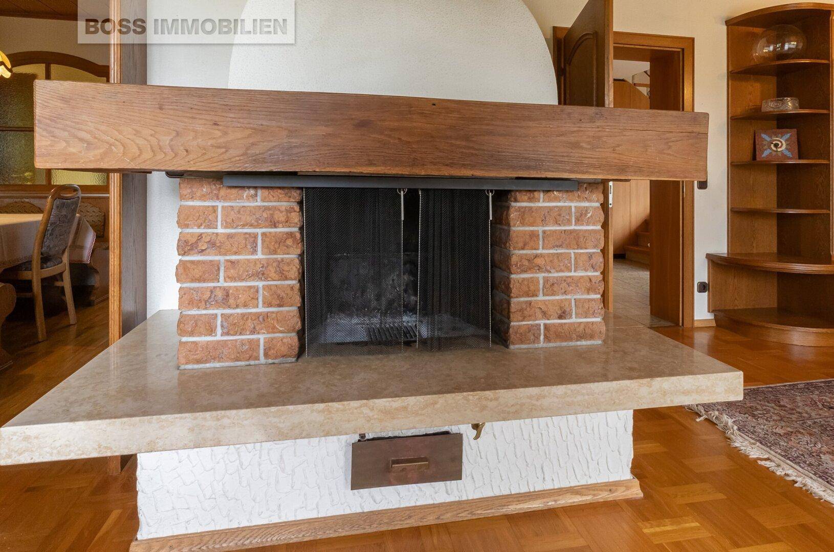Detailansicht des gemauerten Kamins mit Holzmantel und heller Steinplatte im Wohnzimmer.