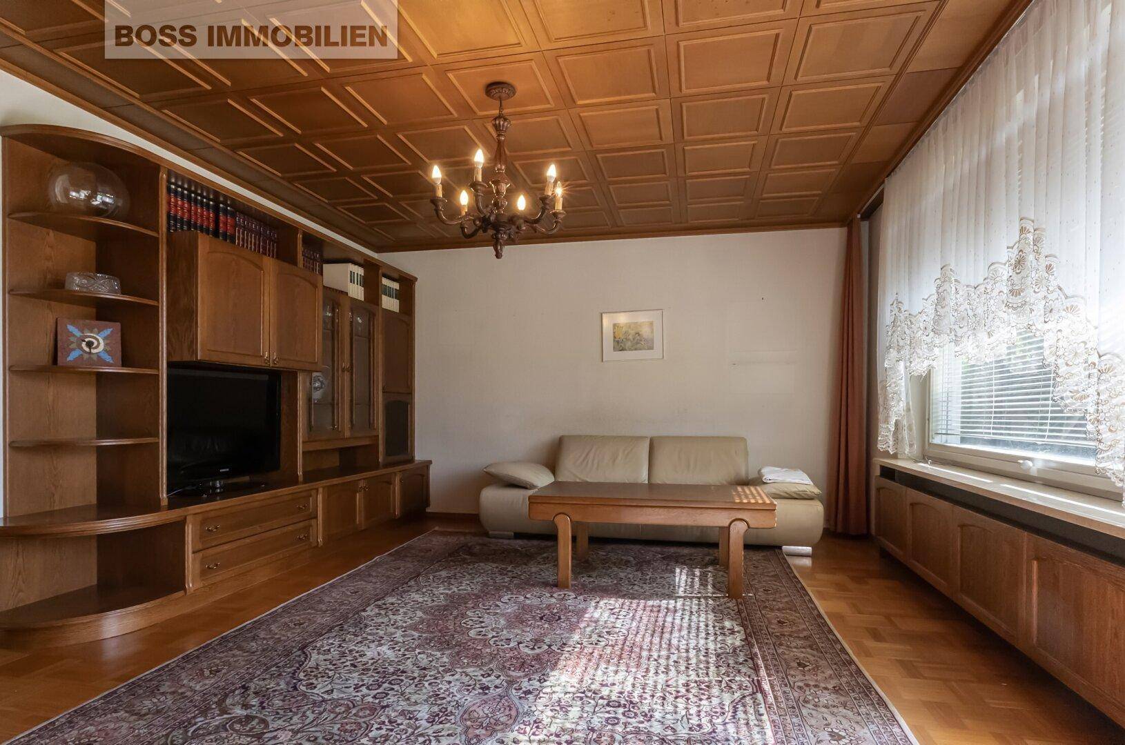 Gemütliches Wohnzimmer mit Holzkassettendecke, Parkettboden und beiger Couch.