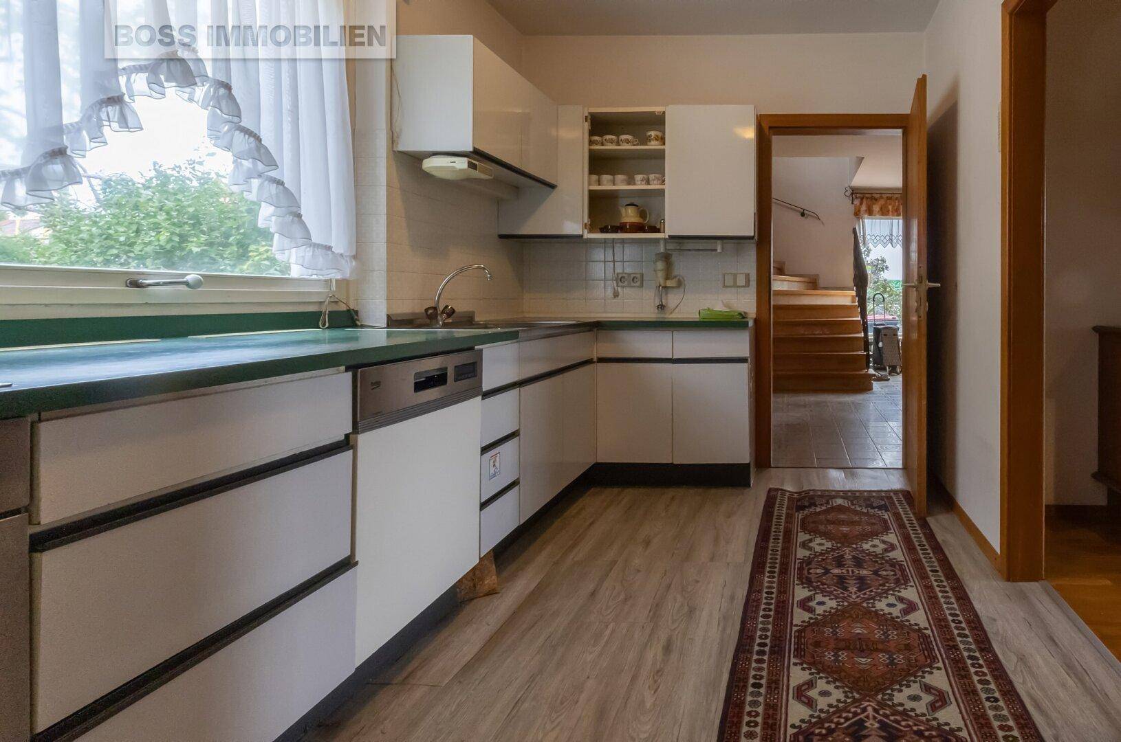 Funktionale Küche mit weißen Schränken, grüner Arbeitsplatte und Blick ins Treppenhaus.
