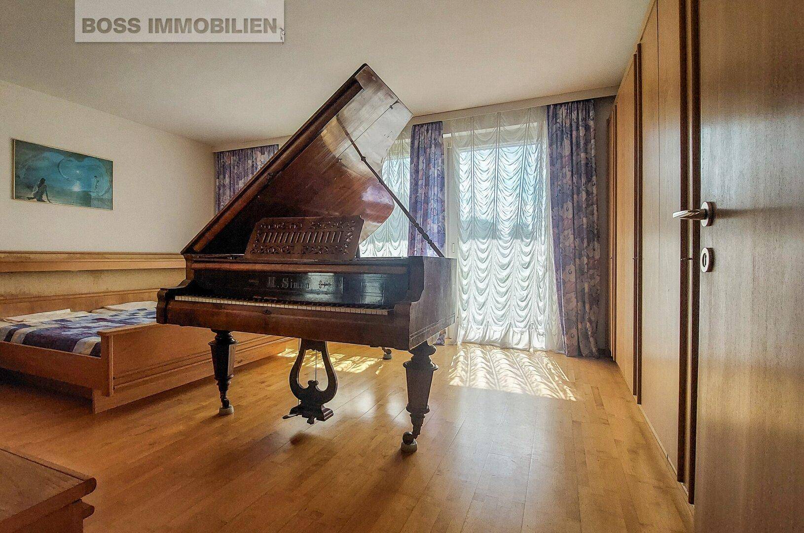 Geräumiges Schlafzimmer mit Holzboden, großem Fenster und einem Flügel.