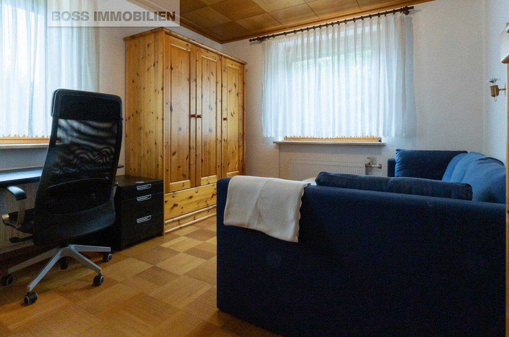Helles Arbeitszimmer mit Parkettboden, Holzschrank und blauem Sofa.