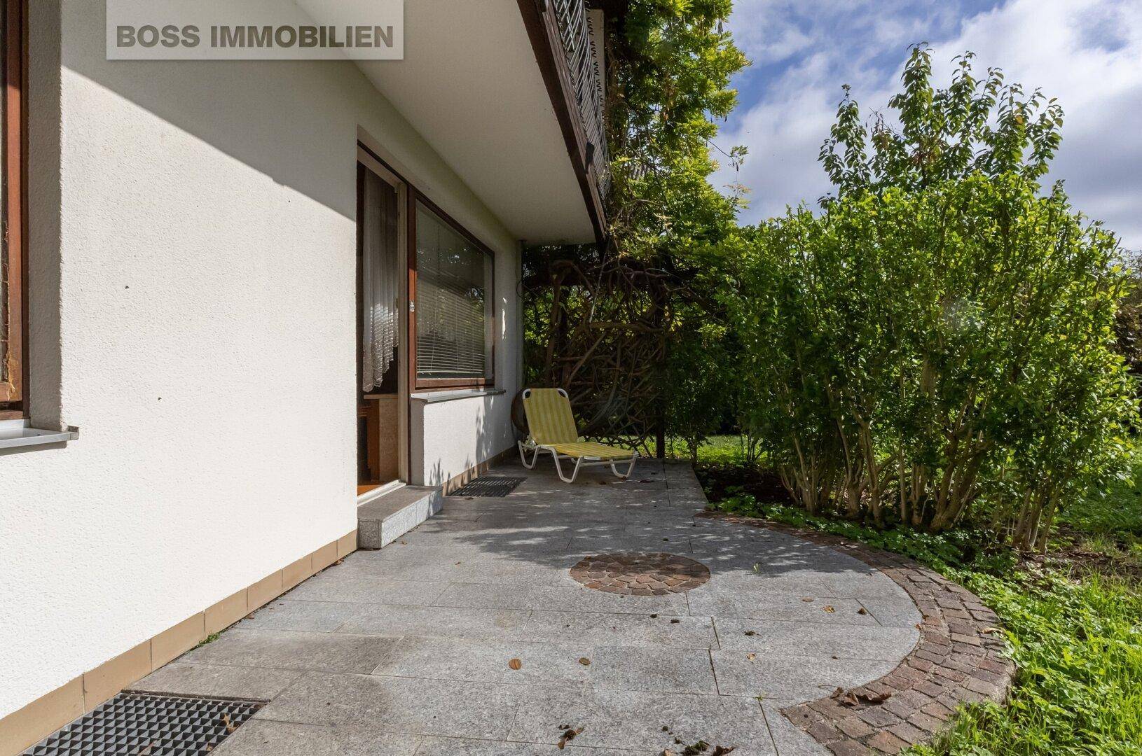 Gepflasterte Terrasse mit Sonnenliege und umgebender Grünfläche.