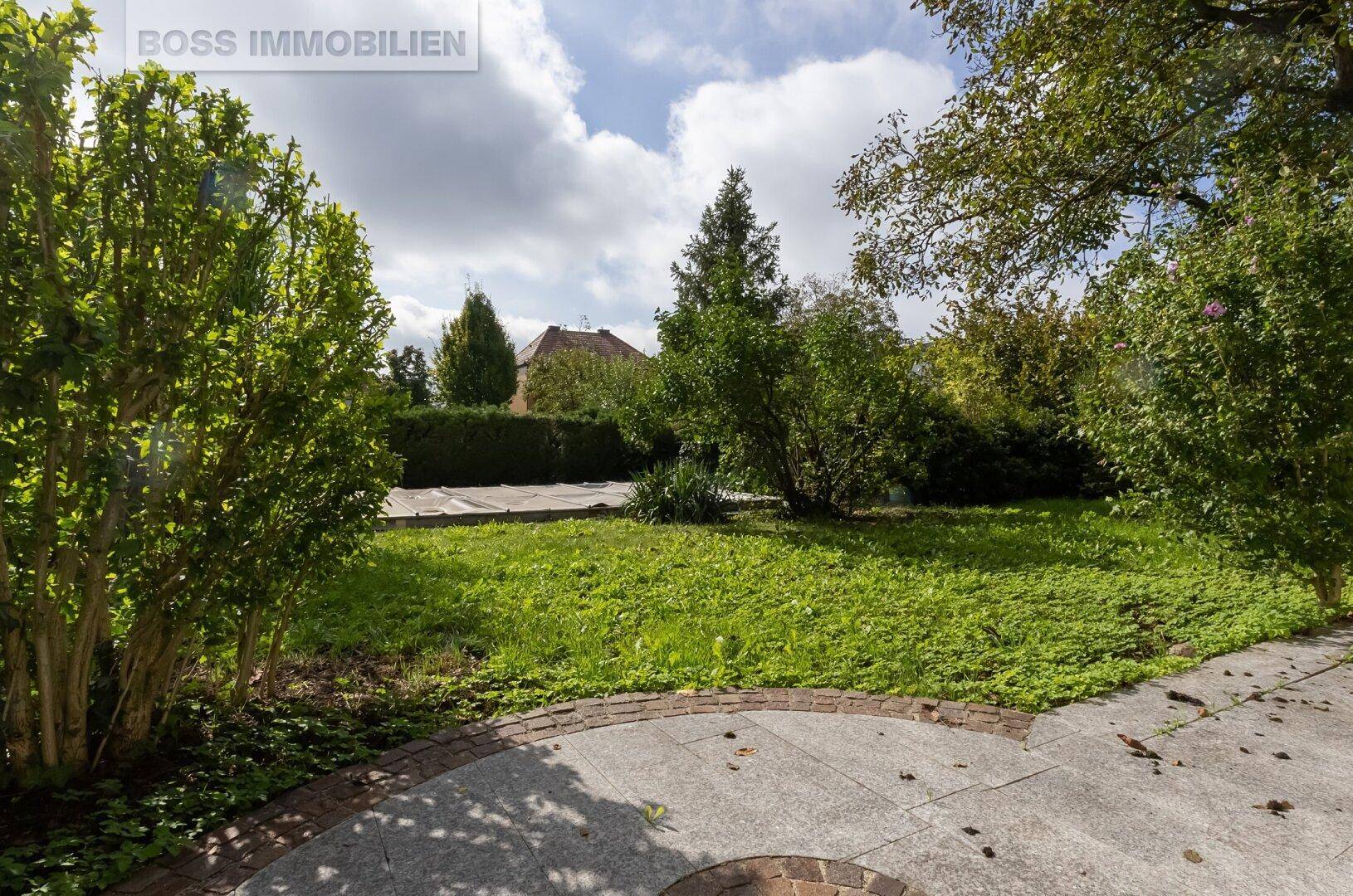 Gepflegter Garten mit Rasenfläche, Sträuchern und gepflastertem Bereich.