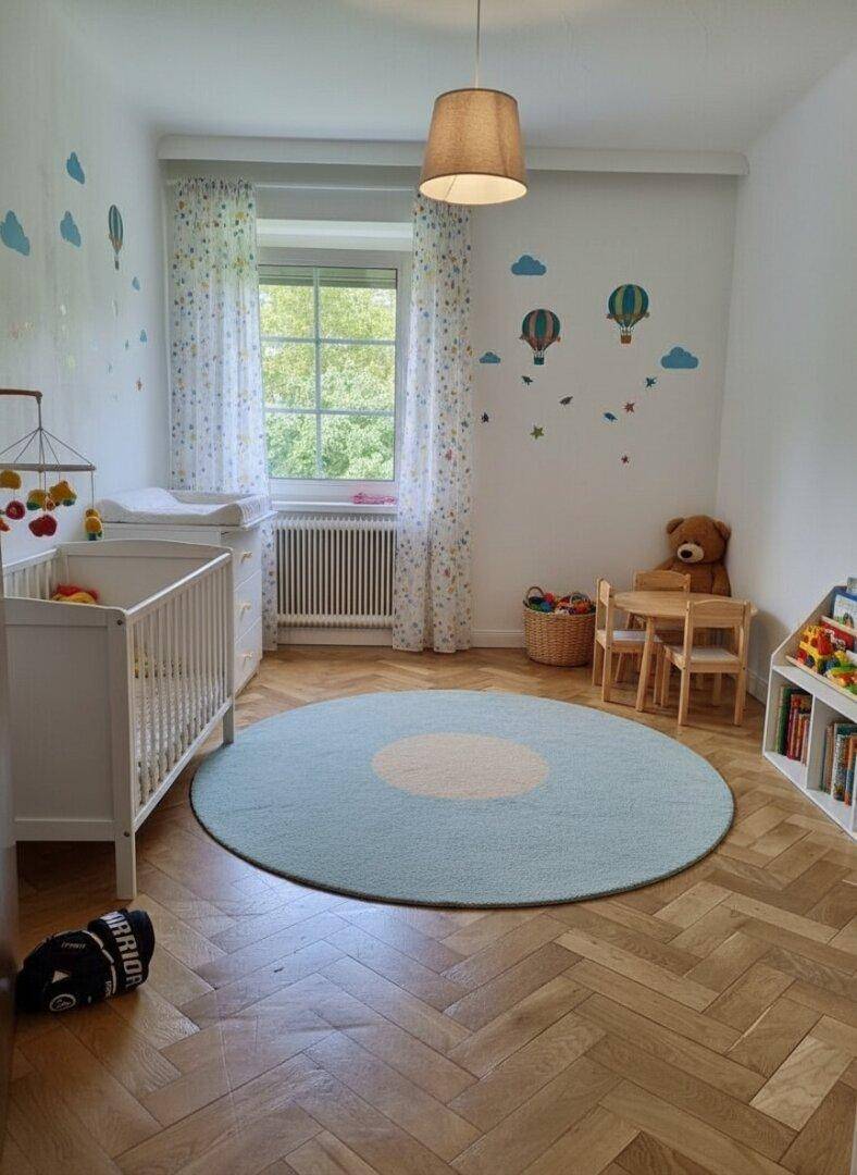 Freundliches Kinderzimmer mit Parkettboden, Babybett und spielerischer Wanddekoration.