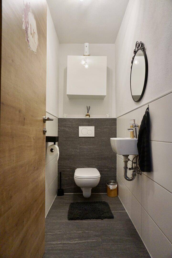 Modernes Gäste-WC mit Wand-WC, kleinem Waschbecken und dunklen Fliesen.