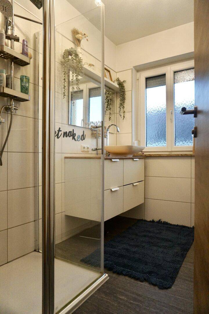 Helles Badezimmer mit Duschkabine, Holzwaschbecken und Fenster.