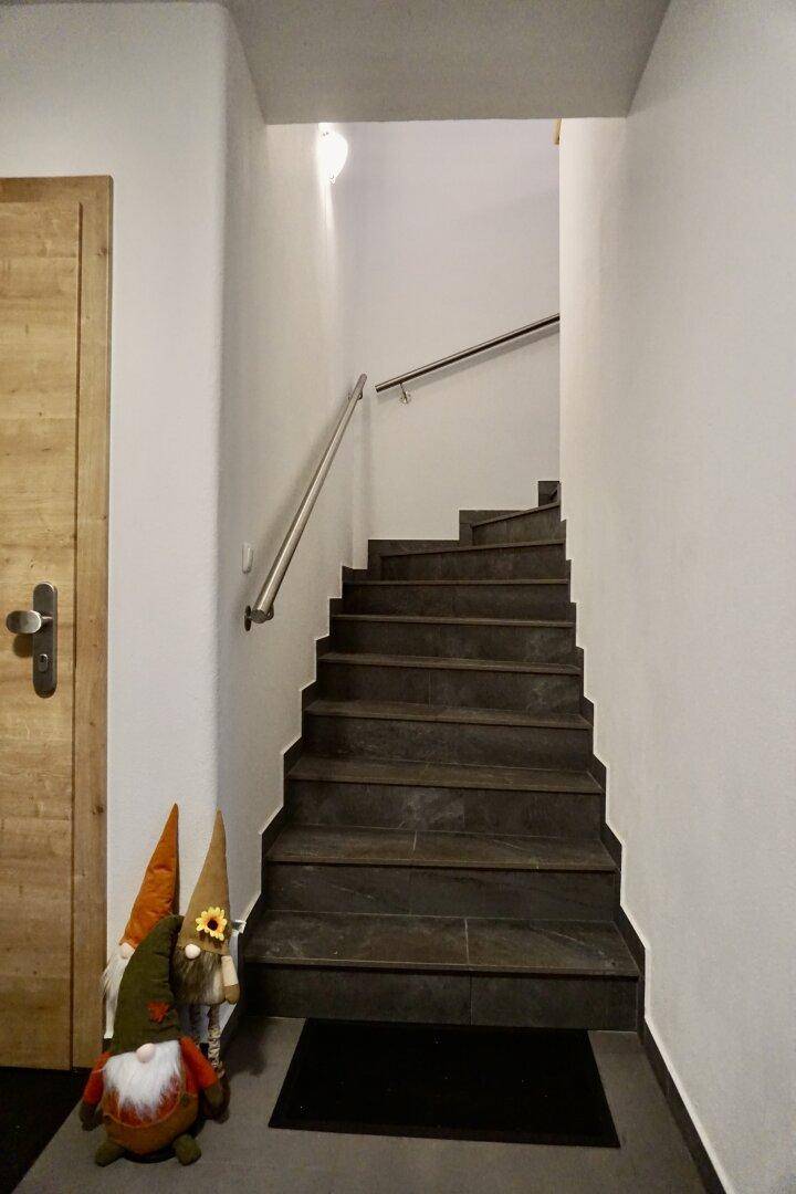 Treppenhaus mit dunklen Stufen, hellem Geländer und dekorativen Gartenzwergen.