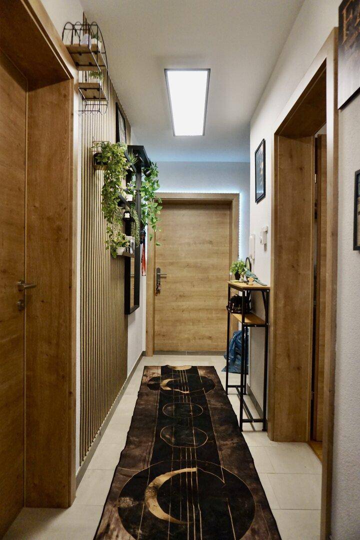 Langer Flur mit Holztüren, modernem Teppich und dekorativen Pflanzen.