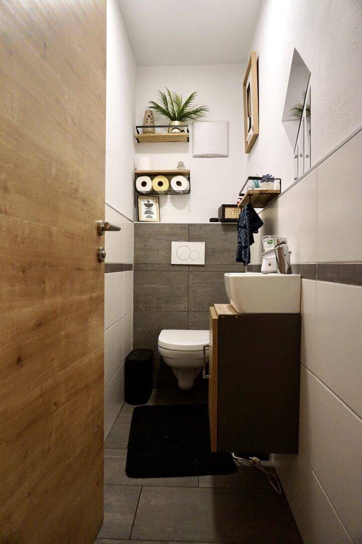 Modernes Gäste-WC mit Wand-WC, Waschbecken und dekorativen Regalen.