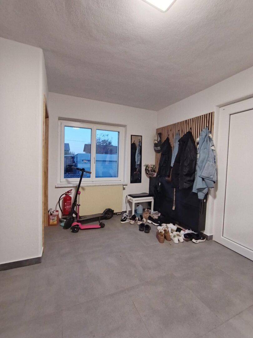 Heller Eingangsbereich mit Fenster, Garderobe und praktischem Schuhregal auf Fliesenboden.