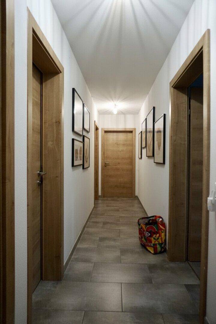 Heller Flur mit grauen Fliesenboden und mehreren Holztüren.