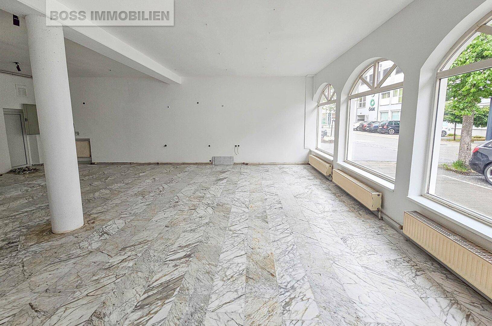 Leerer Geschäftsraum mit Marmorboden und großen Rundbogenfenstern, die viel Tageslicht hereinlassen.