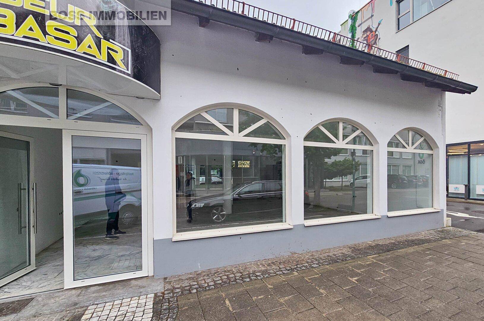 Außenansicht eines Geschäftsgebäudes mit großen Rundbogenfenstern und Eingangstür zur Straße.