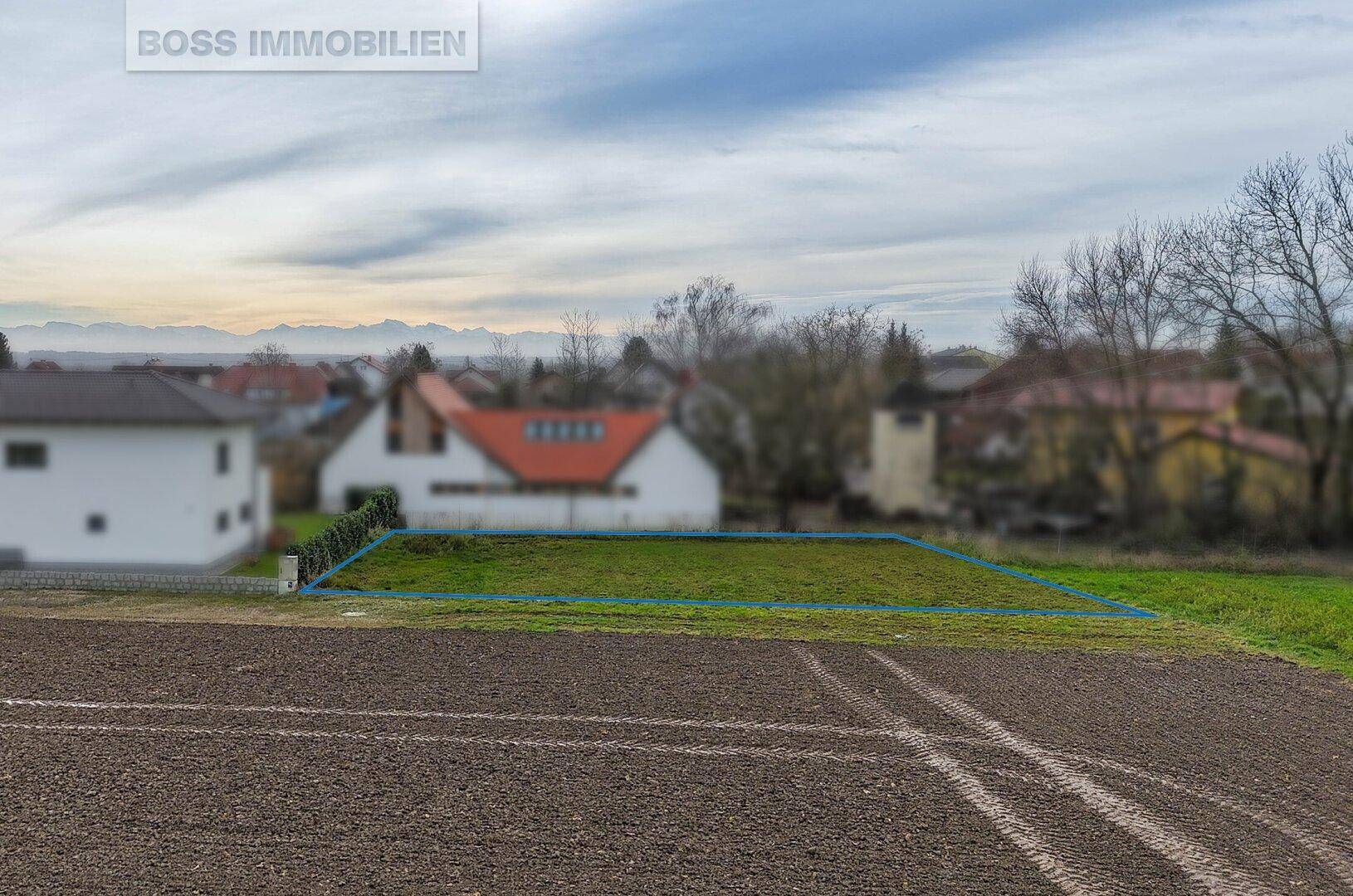 Blick über ein markiertes Grundstück mit Ackerland im Vordergrund und Bergen am Horizont.