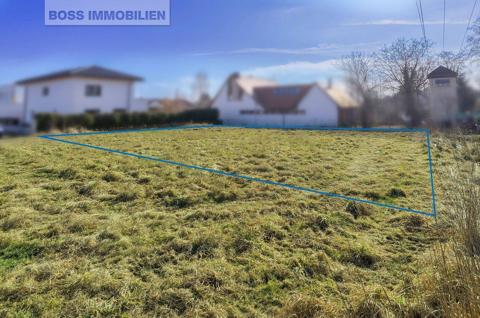 Weitläufige Grünfläche mit markiertem Baugrundstück und Häusern in der Ferne.