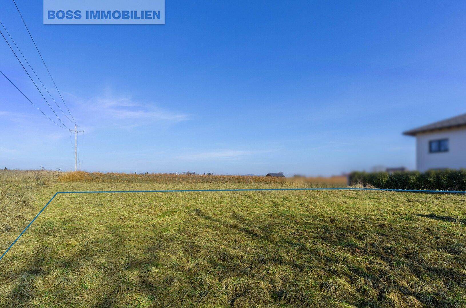 Offenes Feld mit markierter Grundstücksgrenze und Stromleitungen am Horizont.