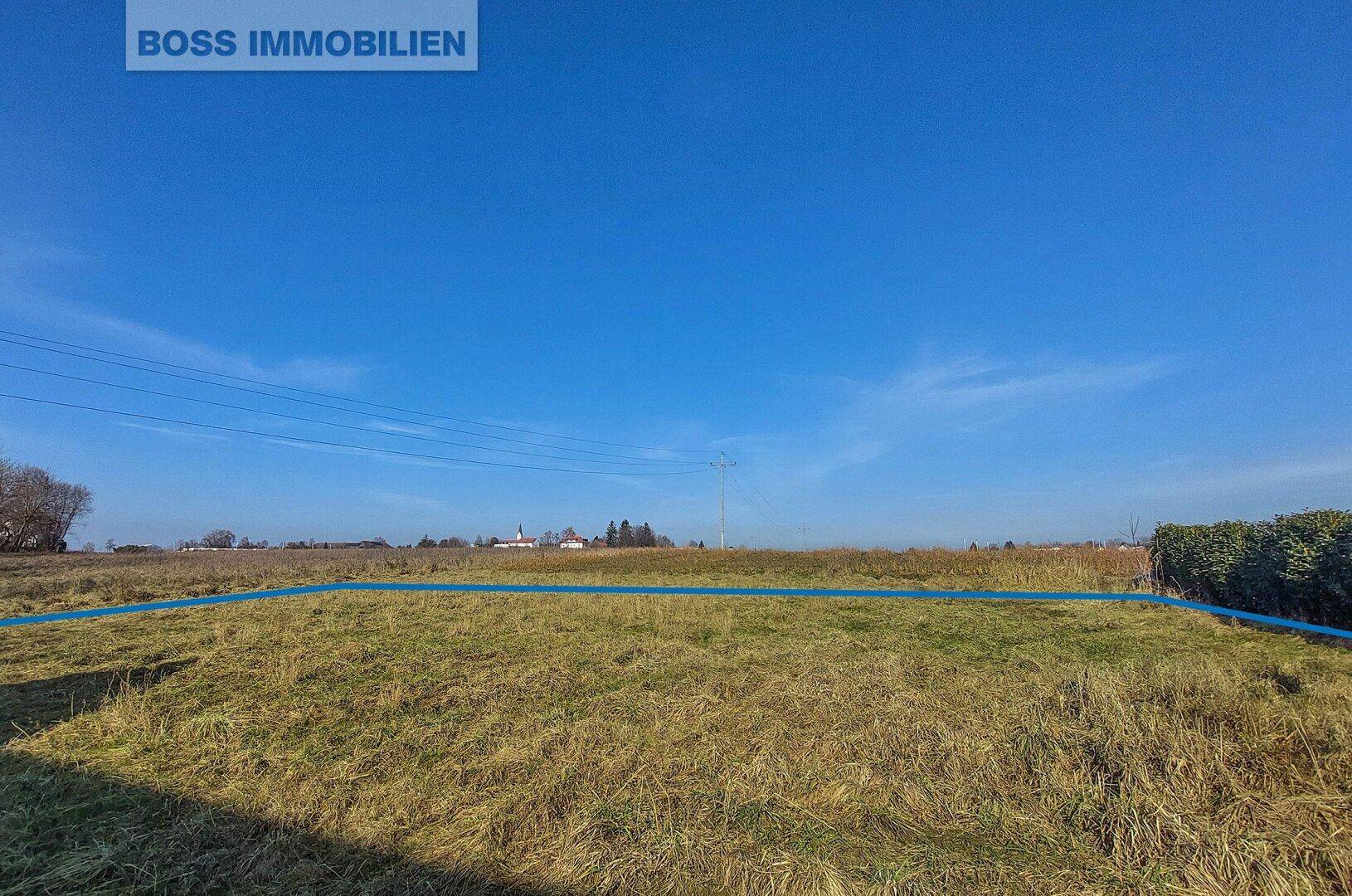 Weite Grünfläche mit markierter Grenze und Strommasten unter klarem blauem Himmel.