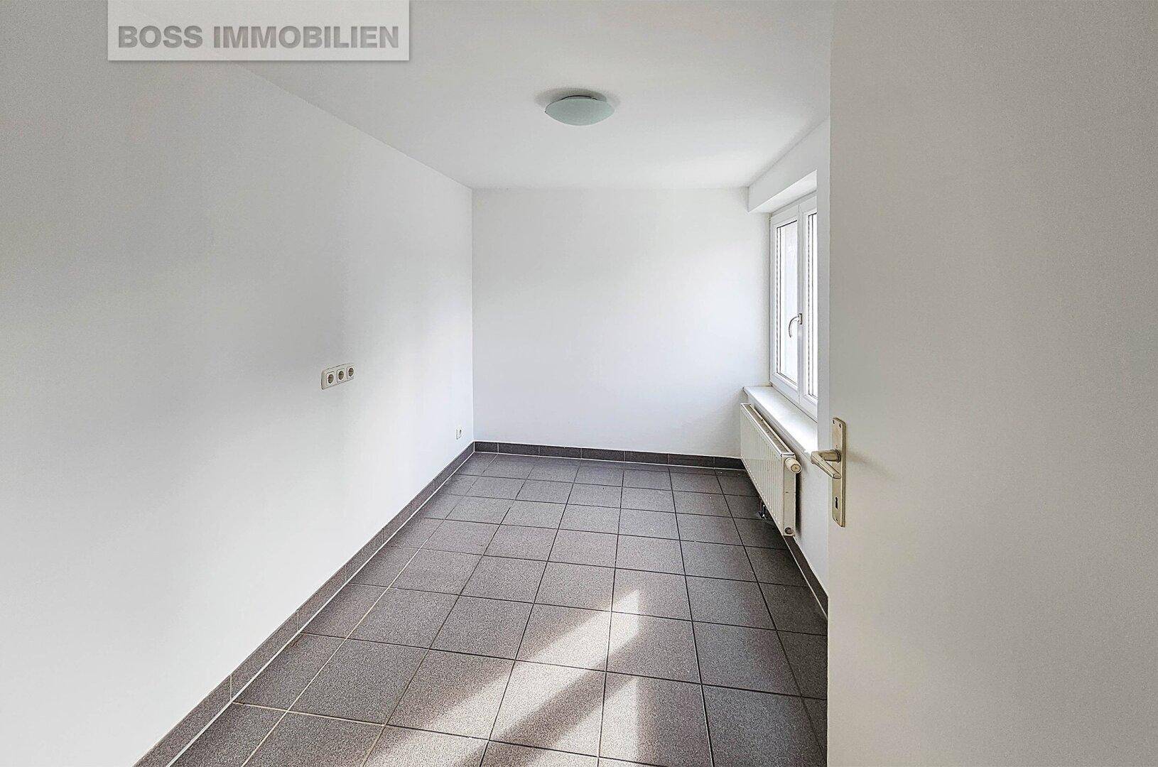 Kleiner, heller Büroraum mit Fliesenboden, weiß gestrichenen Wänden und einem Fenster für Tageslicht.